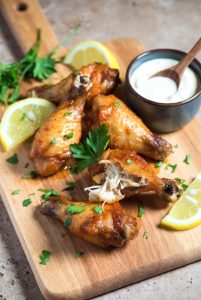 Golden crispy air fryer chicken wings with lemon and parsley on wooden board, juicy inside, no oil added