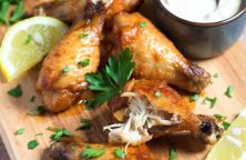 Golden crispy air fryer chicken wings with lemon and parsley on wooden board, juicy inside, no oil added