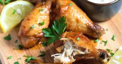 Golden crispy air fryer chicken wings with lemon and parsley on wooden board, juicy inside, no oil added