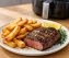 Golden air fryer steak and chips on white plate with rosemary, juicy rump steak and crispy hand-cut chips, air fryer in background