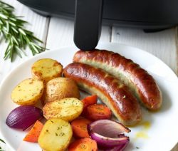 Golden brown sausages with roasted carrots, baby potatoes, and red onion on a white ceramic plate, air fried to perfection