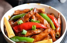 Air fryer Chinese stir-fry with chicken, pork, red pepper, and baby corn in glossy sauce, served in white ceramic bowl