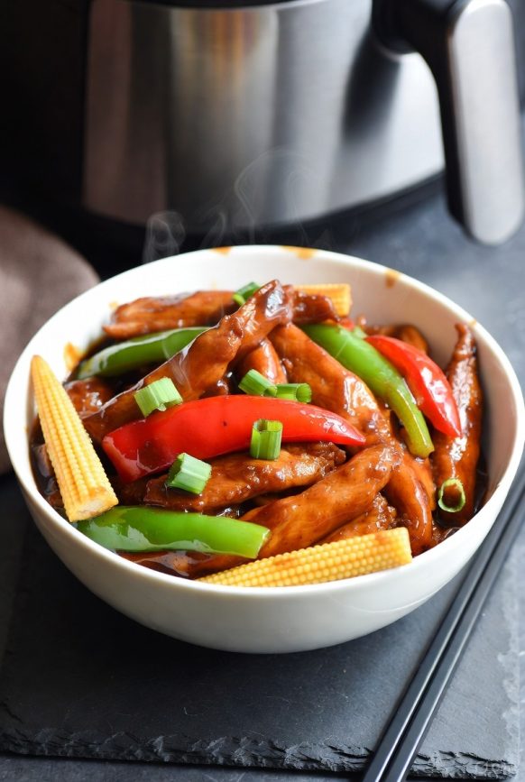 Air fryer Chinese stir-fry with chicken, pork, red pepper, and baby corn in glossy sauce, served in white ceramic bowl